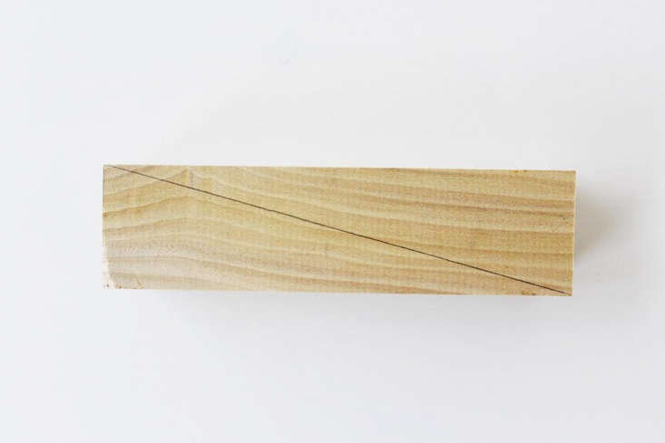 A pencil marking a diagonal line across a wood block for cutting.