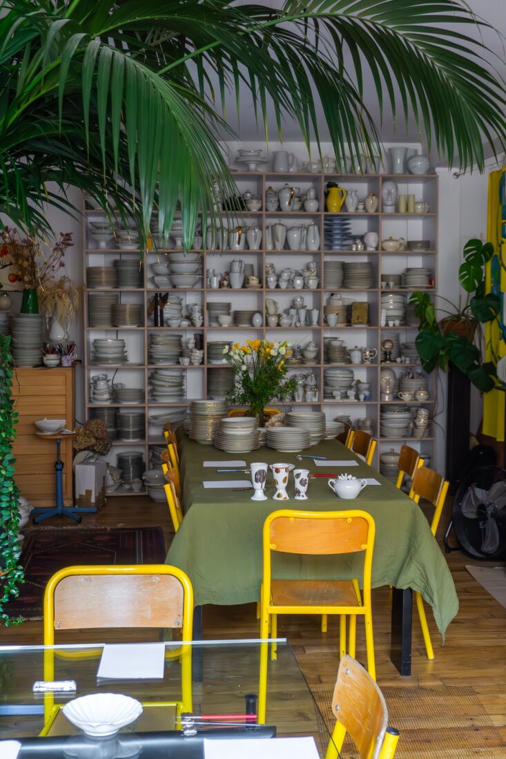 The interior of Arnold’s Paris atelier featuring a large wooden table and shelves of antique porcelain.