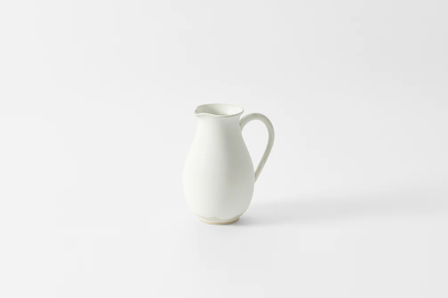 A hand-thrown white beige ceramic pitcher with a smooth finish.