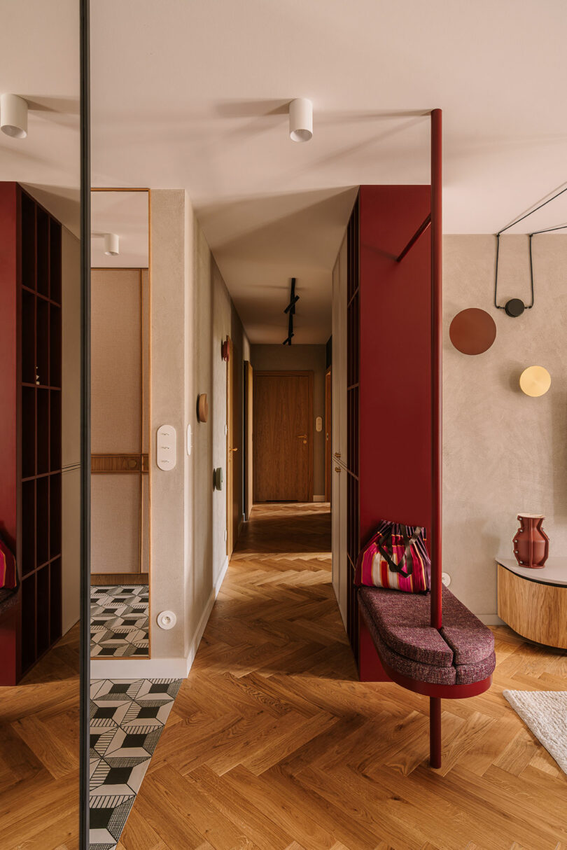 Modern hallway with herringbone wood floors, a maroon seating area, and geometric wall art leading into the living space.