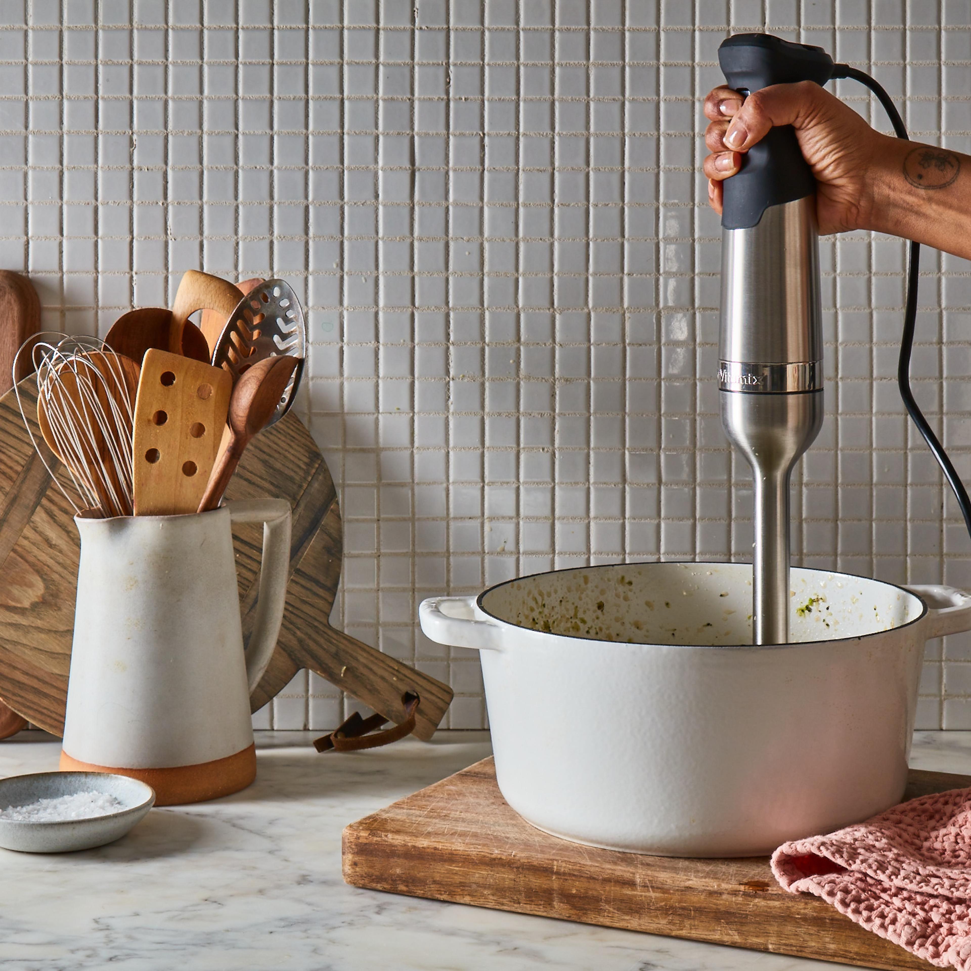 A hand-held immersion blender mixing ingredients directly in a stainless steel bowl.
