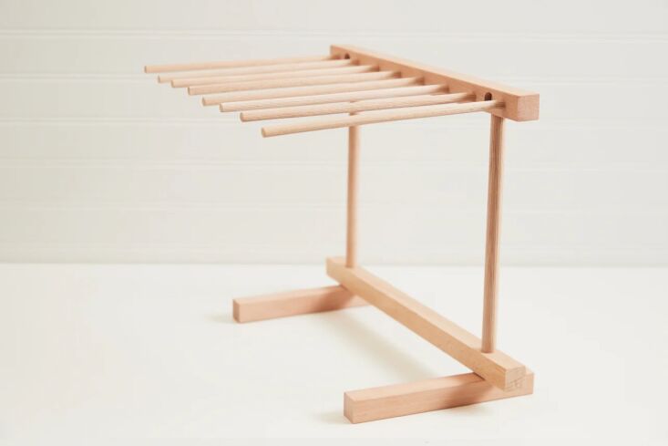 Handmade pasta strands hanging to dry on a multi-tiered beechwood drying rack.