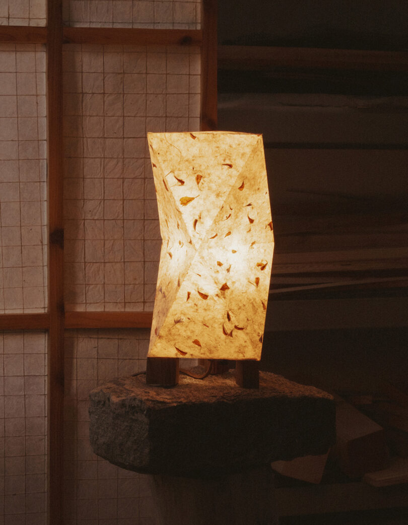 A geometric handmade paper lamp with a warm glow sitting atop a rough stone pedestal.
