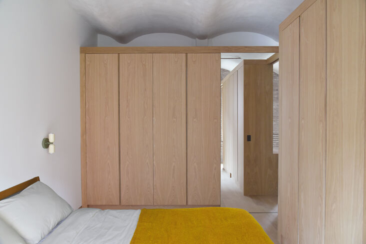 A hallway lined with custom white oak closets and an Up Down Sconce by In Common With.