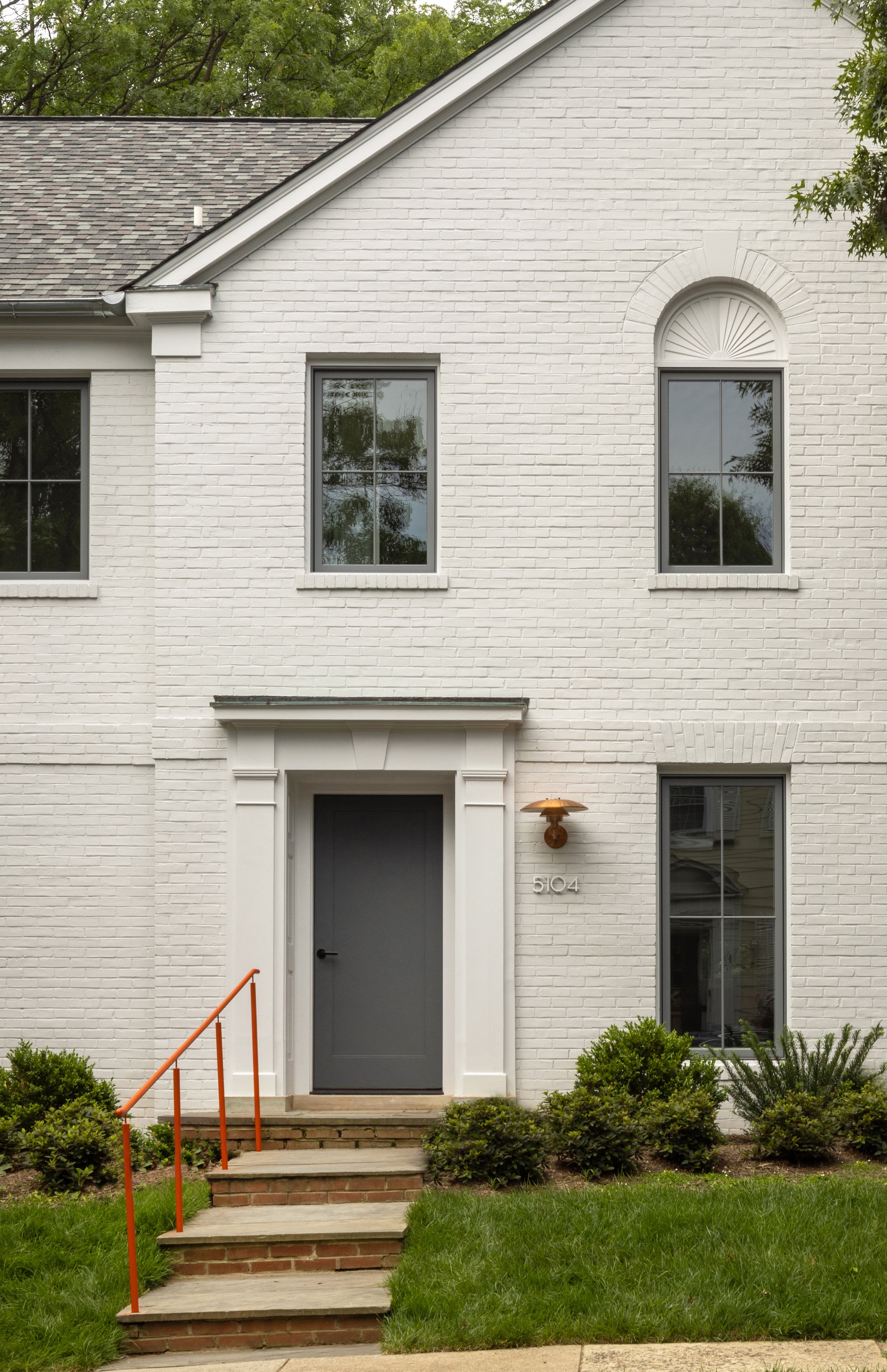 Exterior view of a painted brick house with black window frames, an orange handrail, and a copper wall sconce.