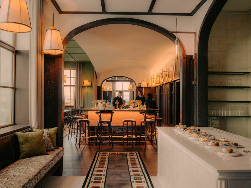 A warmly lit restaurant interior with a central bar, wooden chairs, and arched doorways.