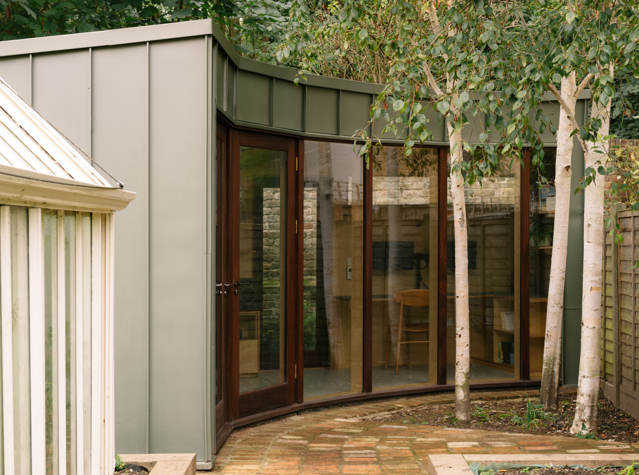 A modern garden room with timber cladding and large glass doors viewed from the exterior garden path.