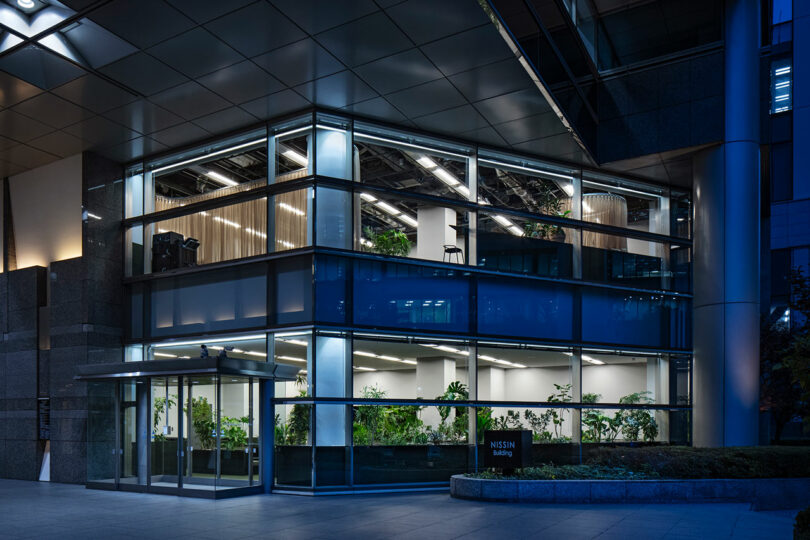 The NISSIN building at night, showing the illuminated two-story KOKUYO DIG office space from the exterior.