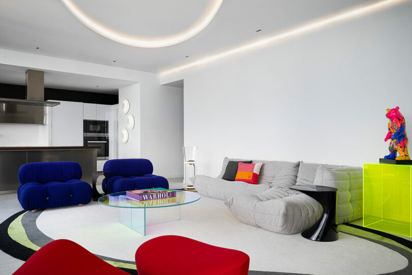 Living area featuring a neon yellow stand with a colorful sculpture, a gray modular sofa, and designer chairs.