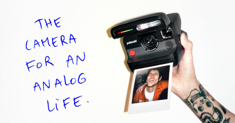A hand holding a freshly printed instant photo with the handwritten text 'THE CAMERA FOR AN ANALOG LIFE'.