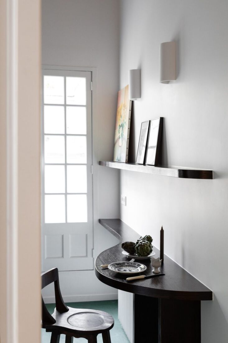 A small built-in dining table under a half-cylinder sconce with an antique walnut chair.