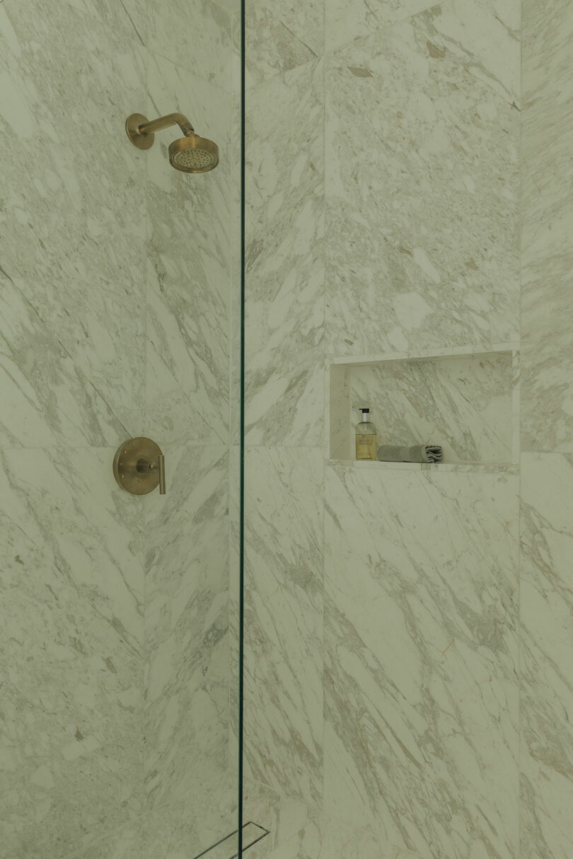 A marble-tiled shower with a minimalist brass showerhead and control.