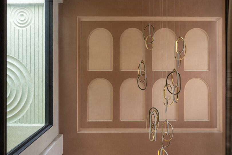 A wall with arched recesses and a gold ring chandelier, showcasing textured circular patterns on the surface.