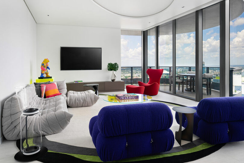 Modern living room with vibrant blue and red chairs facing a large window with a view of the Miami skyline.