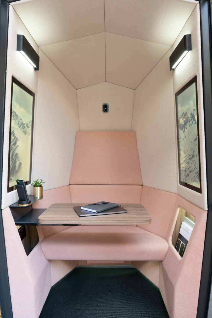 Interior of a small Kabin office booth with a cushioned seat, nature-themed wall art, and warm lighting.