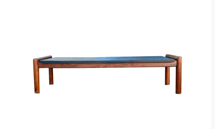 A vintage coffee table with a dark slate top and wooden frame.