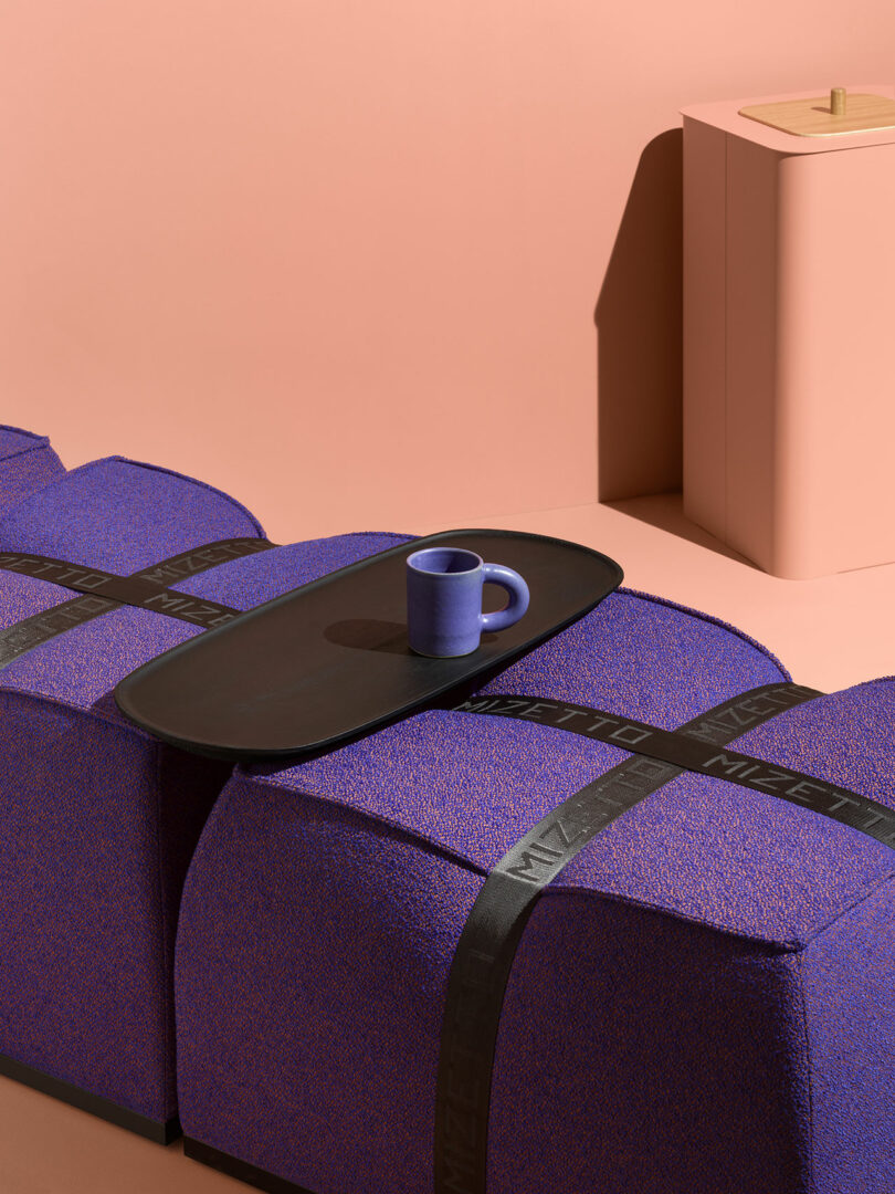 A close-up of purple textured fabric on modular blocks with a black tray and mug.