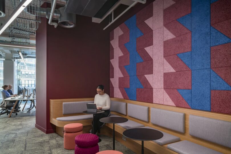A person working on a laptop in a quiet, cushioned booth with geometric wall panels.