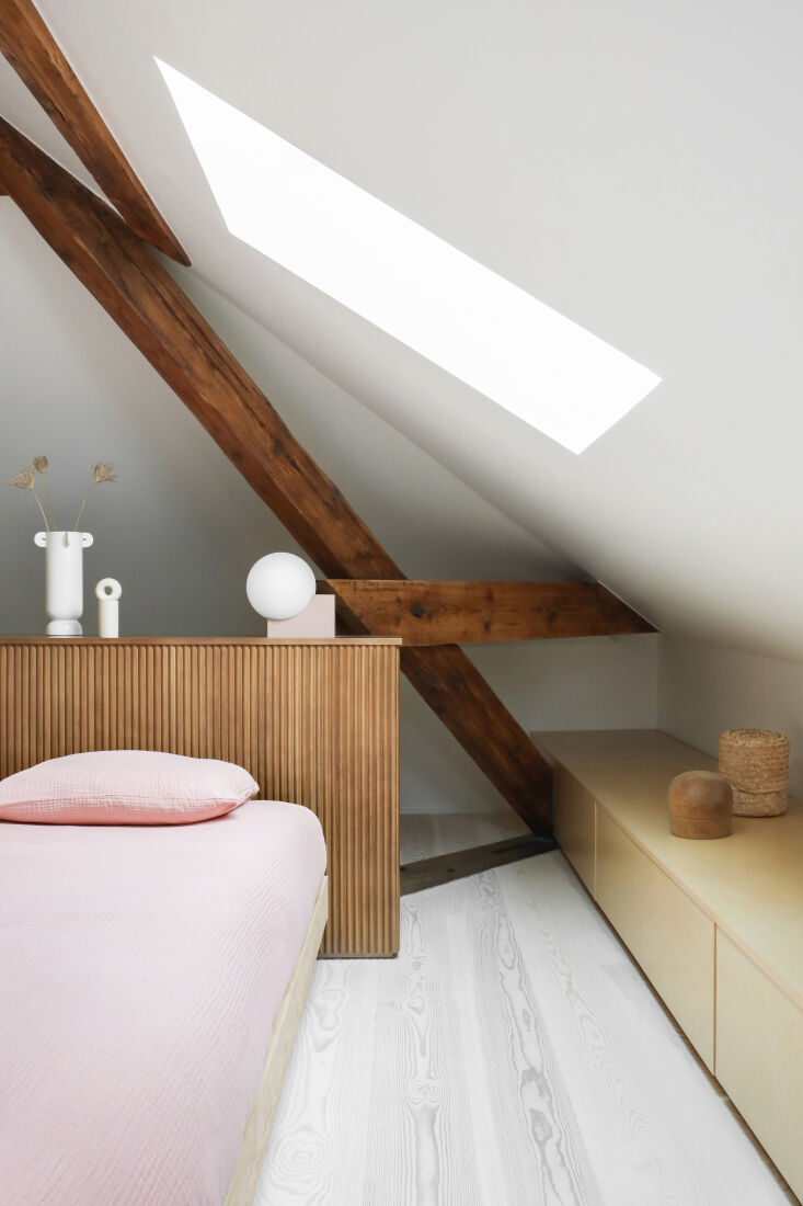 Wooden fluted headboard in a bedroom with integrated storage niches and a skylight above.