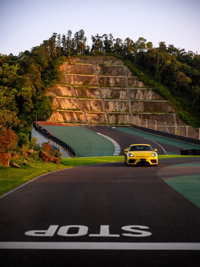 A yellow sports car navigating a turn on the Magarigawa circuit with terraced hills in the background.