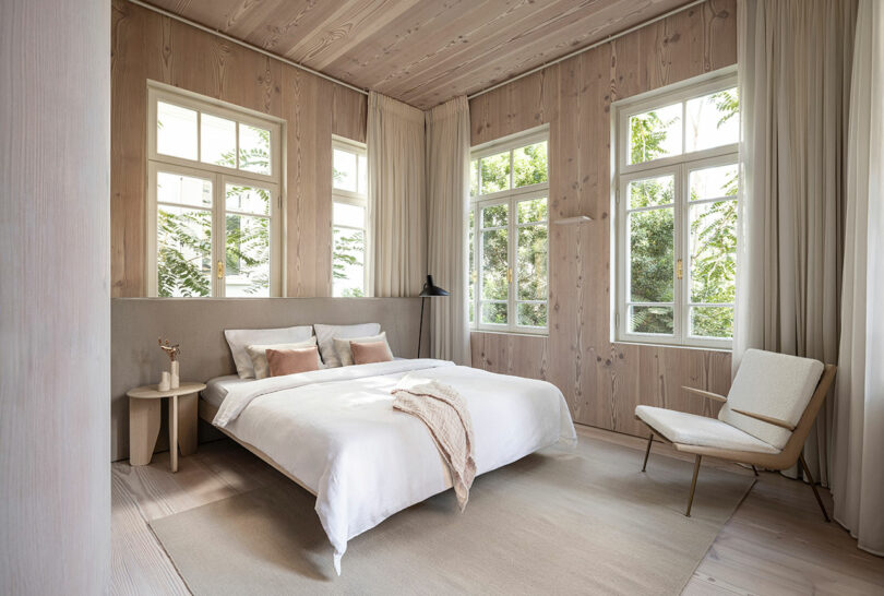 A serene bedroom featuring neutral tones and a floor-to-ceiling window that brings nature into the living space.